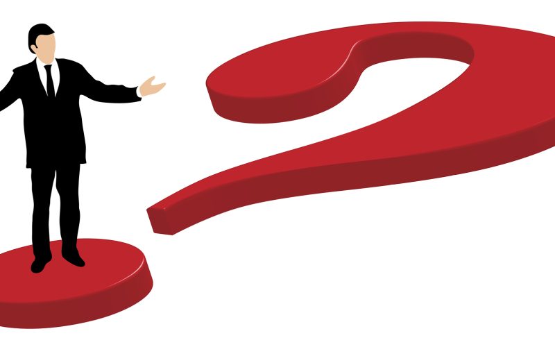 Well dressed business man standing on a big red 3d question mark explaining and gesturing with hands and arms stretched out to the sides.
