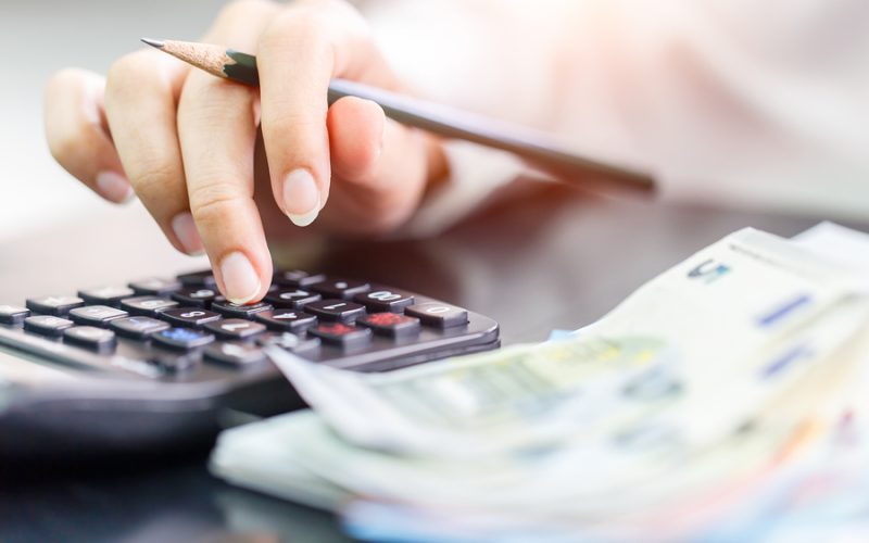 Close up right hand female using calculator in Euro banknotes background. Calculation at home
