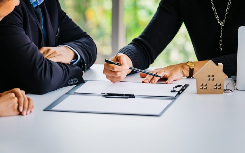 Close-up of married couple signing contract paper alongside with female agent - real estate, housing and residential finance, legal ownership concept